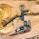 Aerial view of a quarry with a survey drone flying above, showcasing the rugged terrain and heavy machinery below.
