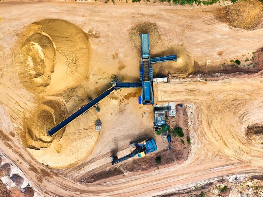 Aerial view of a quarry with a survey drone flying above, showcasing the rugged terrain and heavy machinery below.